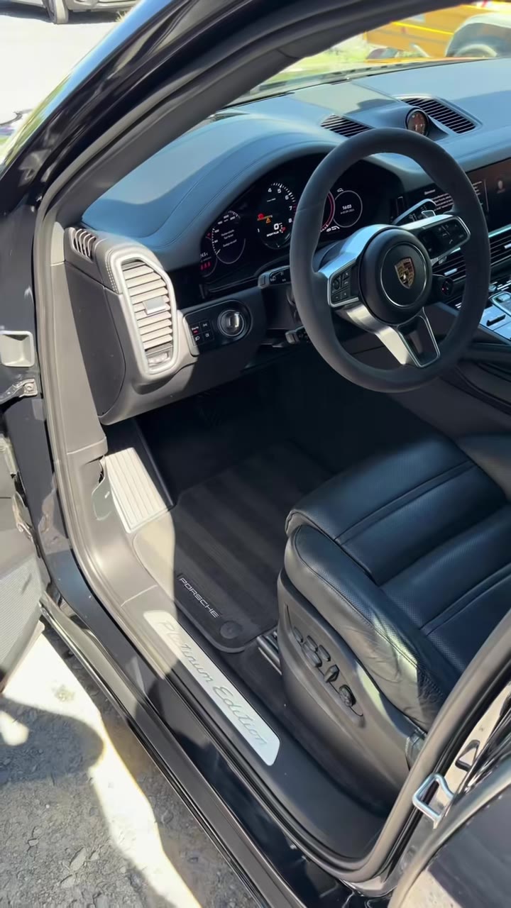 Intérieur d'une Porsche Cayenne : volant, tableau de bord, siège avant en cuir noir, tapis et seuil de porte