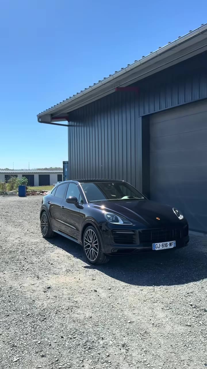 Porsche Cayenne noire vue de trois quarts avant, jantes à branches fines, garée près d'un bâtiment à Lons